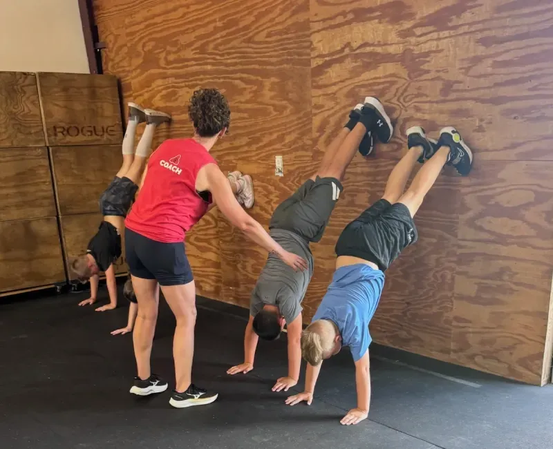 Coach helping a child with a wall walk at CrossFit Northwest Arkansas